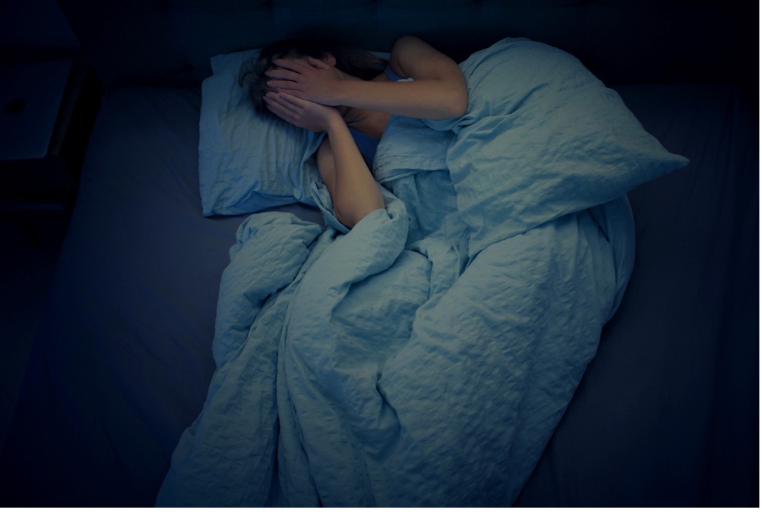 A woman struggles to sleep in a cozy bed, surrounded by soft pillows and blankets, illustrating the connection between sleep and ADHD.