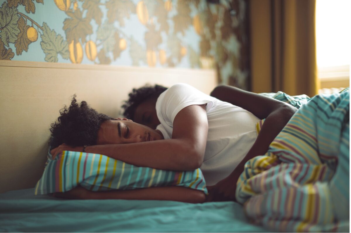 A man and woman sleep side by side in a cosy, comfortable bed, illustrating how sleeping positions can affect sleep quality.