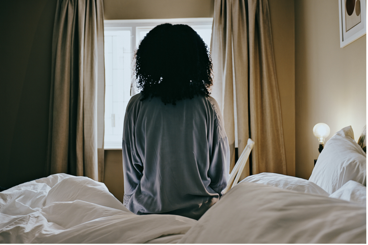 A woman is seated rigidly on the edge of a bed after a restless night, staring at a window, illustrating the link between sleep and mental health.