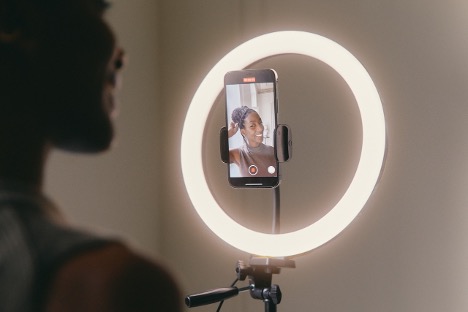 A woman poses for a selfie using a smartphone, with a radiant light ring providing flattering illumination, illustrating how to build confidence.