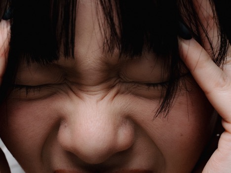 A woman with her hands on her head as she experiences the discomfort of tinnitus or ringing in the ears.