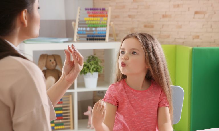 Young girl working with occupational therapist, mimicking the therapist's pursed lips to enunciate speech